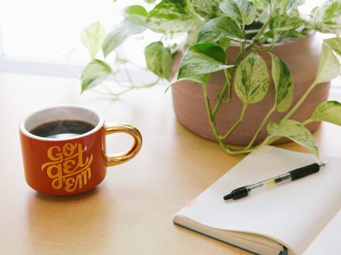 stylo rétractable noir sur un livre ouvert à côté d'une tasse à café imprimée go get'em rouge et blanche