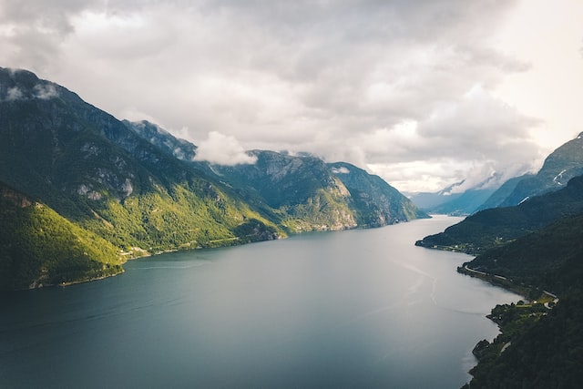 montagnes verdoyantes à côté d'un plan d'eau sous un ciel nuageux pendant la journée